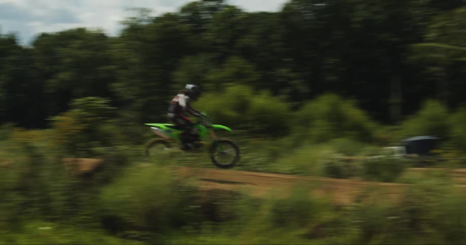 A motorbike travels fast on a rural dirt road flying over hills and into the woods