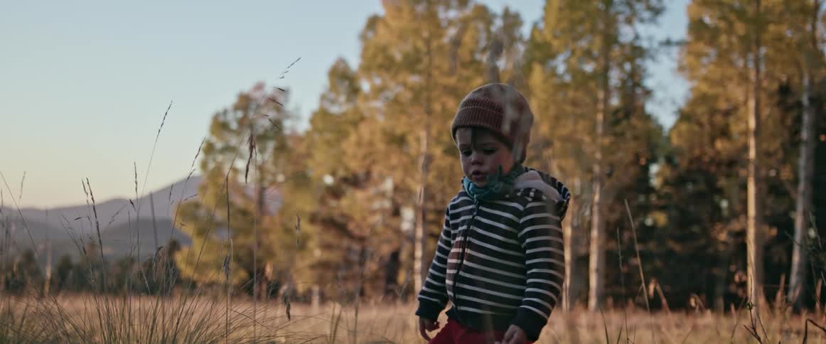 Boy walks across field near woods with mountains in the background