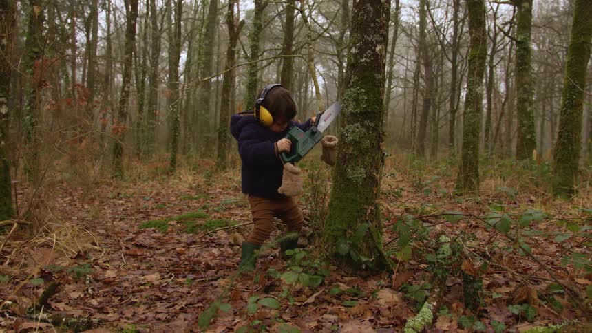A child pretends to use a chainsaw on a tree in the forest