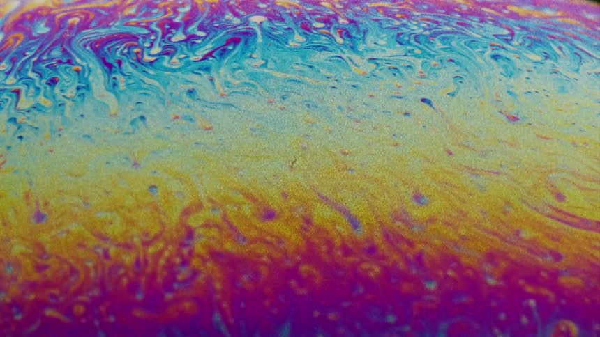 Fluorescent colors move and streaks stretch and blend as small particles float over the surface colors