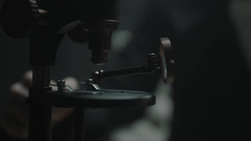 A hand is making an adjustment on an old-style microscope