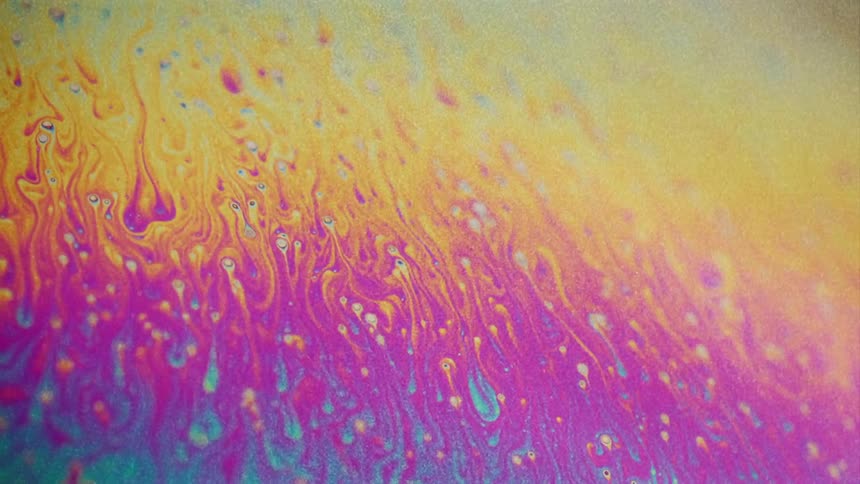 Fluorescent colors move and streaks stretch and blend as small particles float over the surface colors