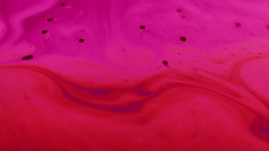 A hot pink and red organic liquid substance moves and blends as particles move across the surface