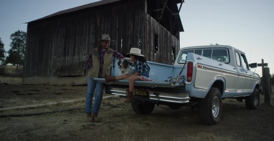 A girl sits with her dog in the bed of a pickup truck while chatting with her dad