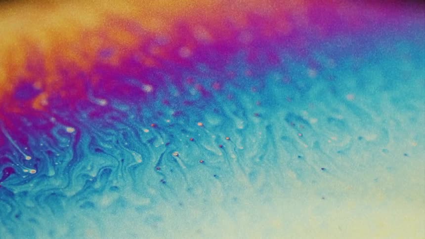 Fluorescent colors move and streaks blend as small particles float over the surface colors