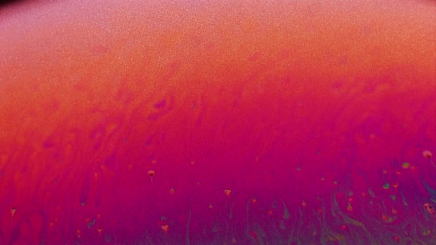 Fluorescent colors move and streaks blend as small particles float over the surface colors as they turn deep red and magenta