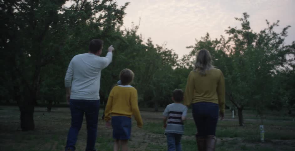 A man points toward the sky while walking through the woods with his family
