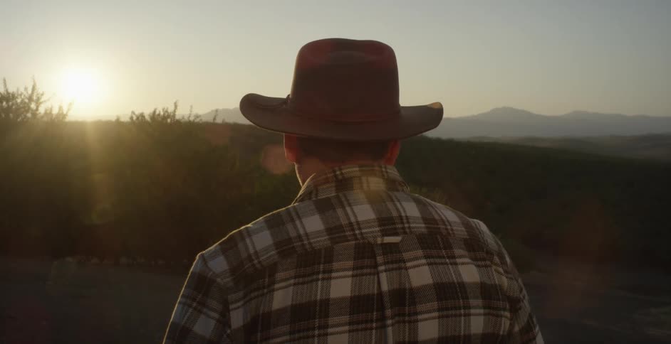 A man is standing outdoors and wearing a cowboy hat
