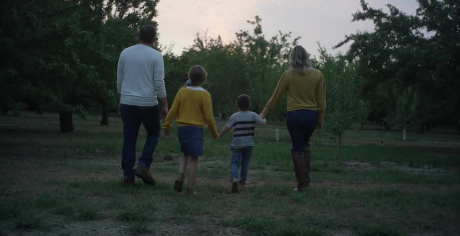 A mother holds her sons hand as they walk with the daughter and husband through and orchard