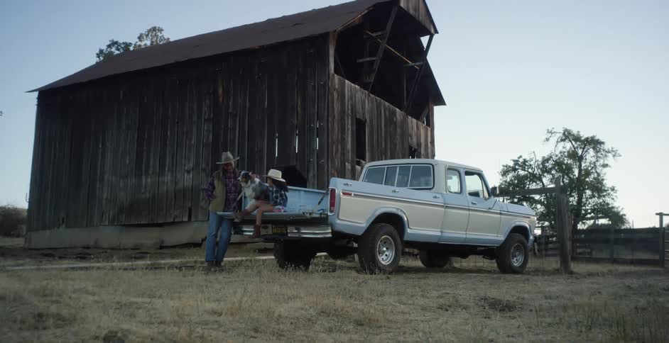 A child and dog sit on the tailgate of a truck talking to an adult man