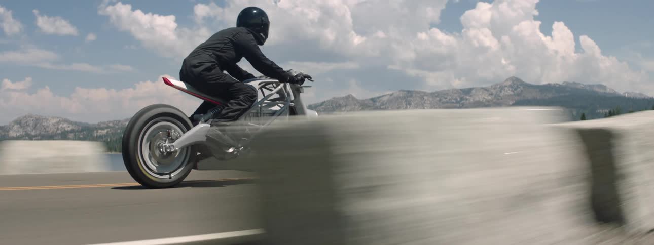 A person in all black riding a motorcycle down a road with mountains in the background