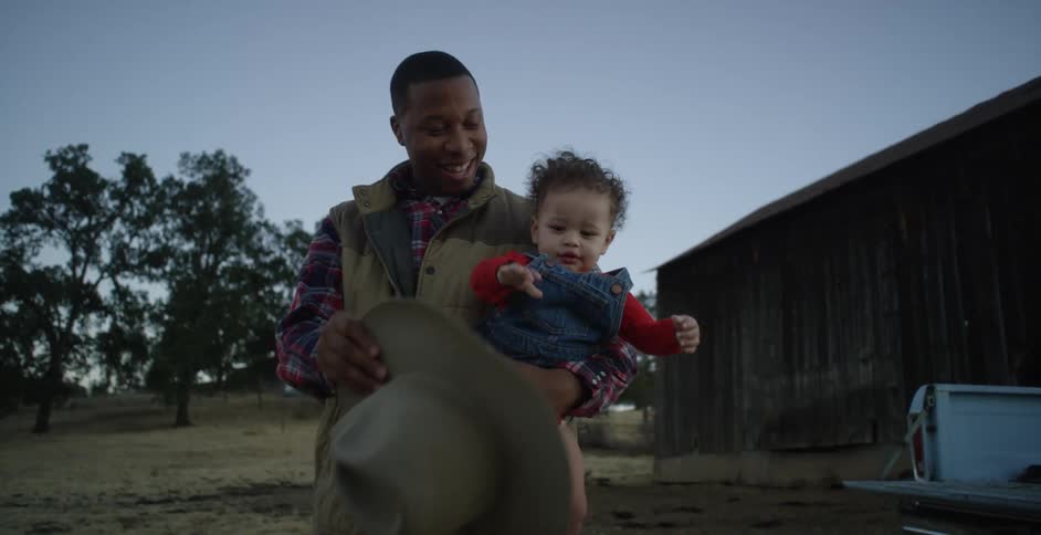 A child with a cowboy hat over her face and the man holding her takes it off and puts it on his head