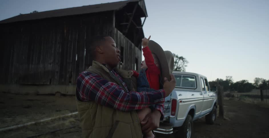 A child in a mans arms as he puts a cowboy hat on her head