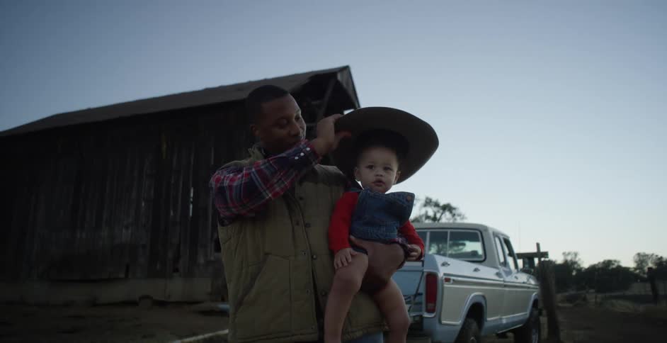 A man wearing a cowboy hat holding a little girl and placing the hat on her head