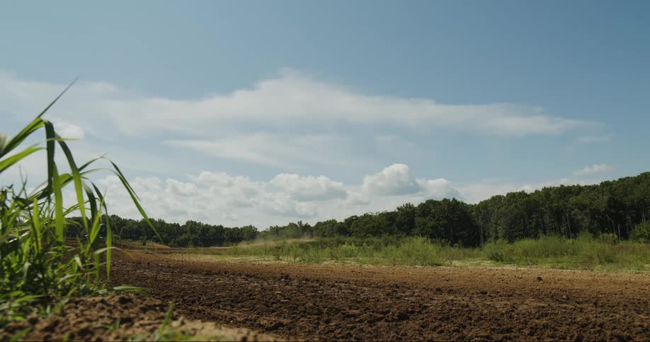 Motorcyclists rides along dirt road near woods on cloudy day