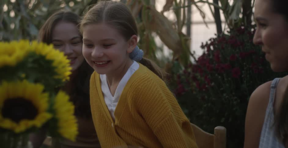 Women greet girl arriving at table with smiles