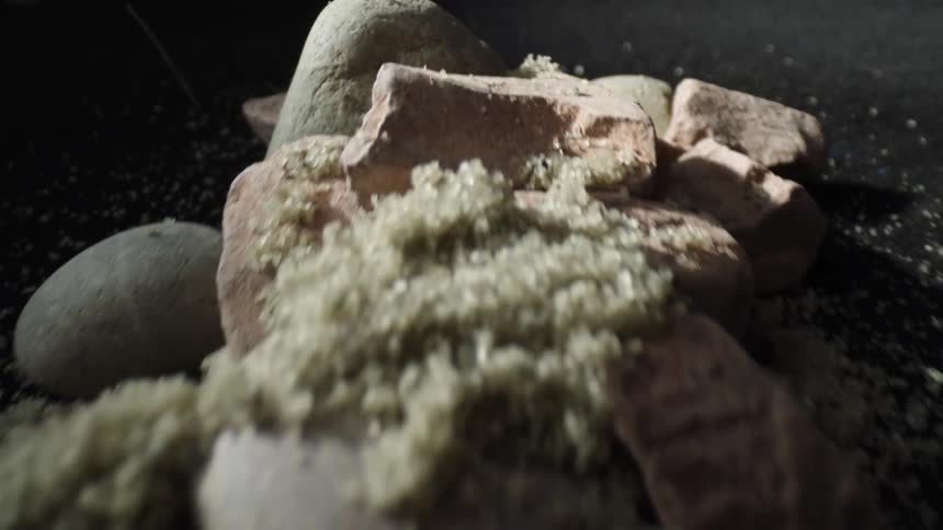 Close up shot of grains of sand falling on some pink light brown and gray rocks