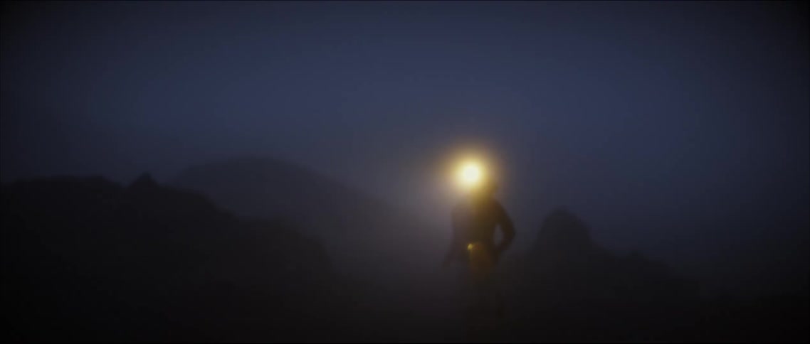 Woman wearing a headlamp jogs through foggy terrain at night
