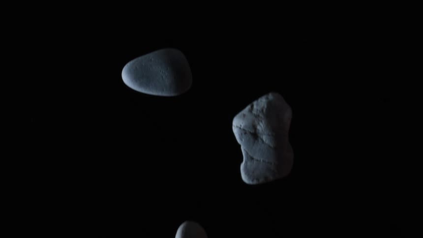 Light shines on rocks as they are tossed up in the air and turn as they fall down in the darkness