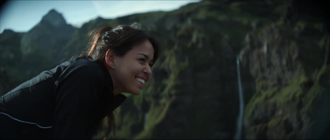 Woman laughs standing across canyon from waterfall