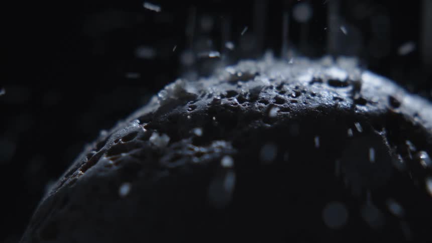 White grains hit and bounce off craggy dome shape in the dark