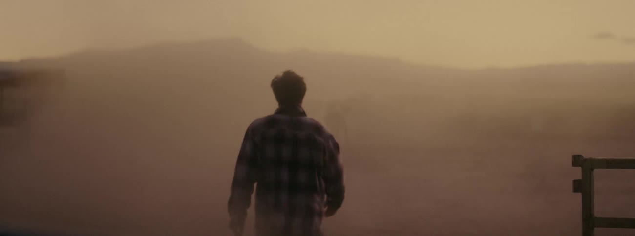 A man walking out from a fence into a dusty area