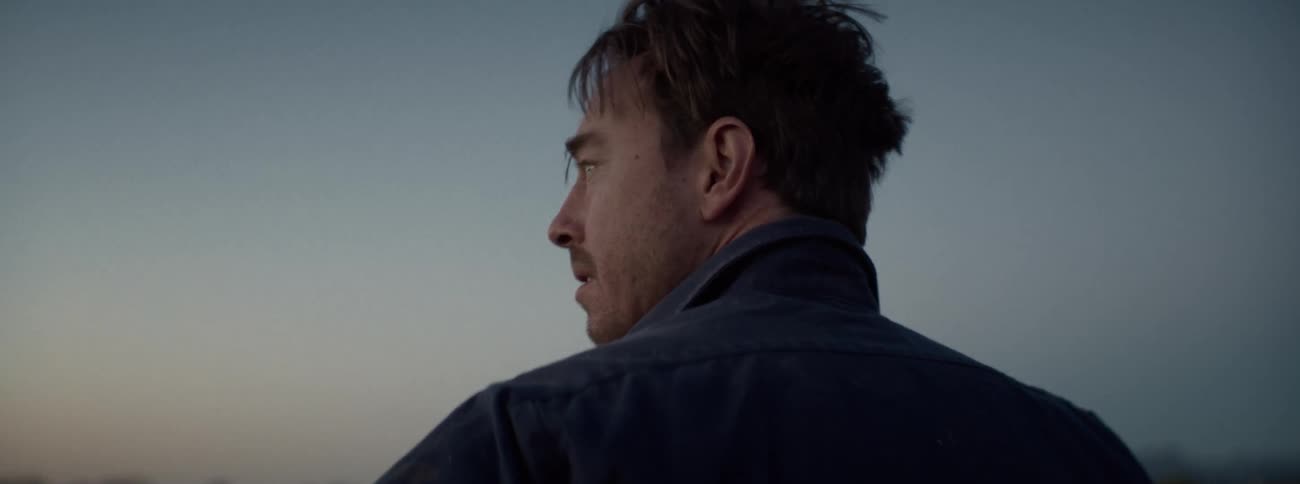 A crying man is standing outside at sunset then turns to his left gazing in the distance