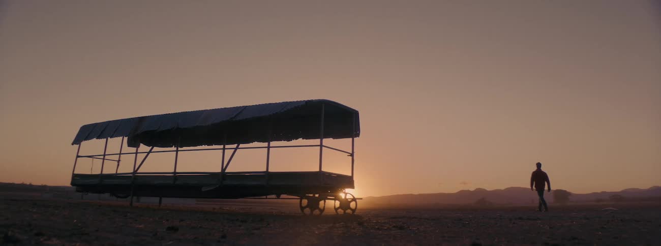 The silhouette of a man can be seen as he walks past an abandoned trailer in a desert area