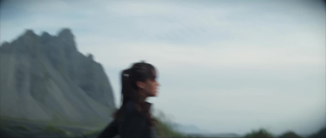 Woman runs across dark dirt with mountain in the background