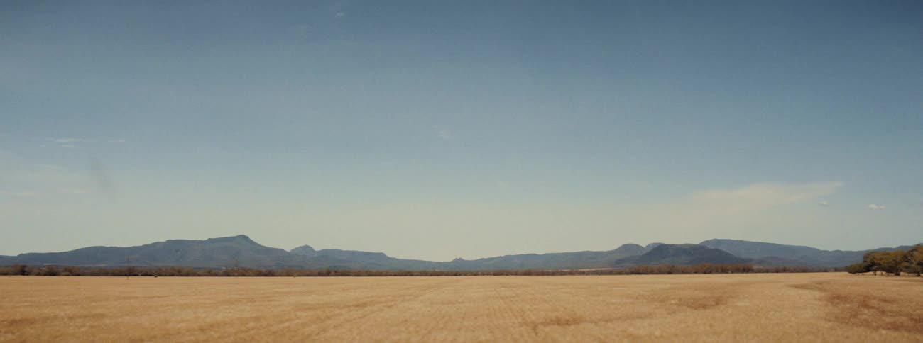 Wide open view of a dry field and mountains in the distance