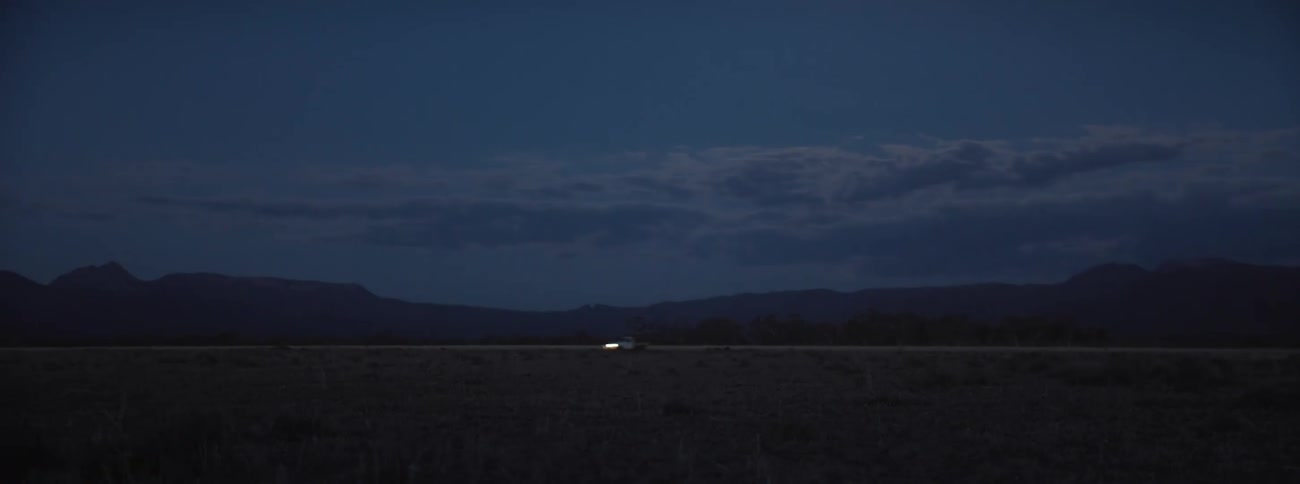 Car drives along road with silhouetted mountains in the background at night