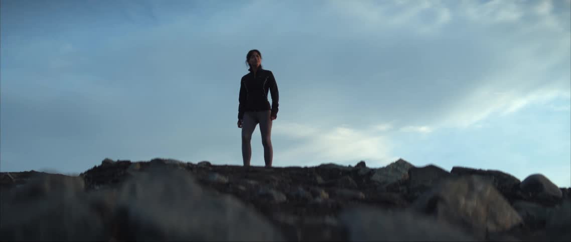 Woman standing on mountain ridge looking out turns and starts running