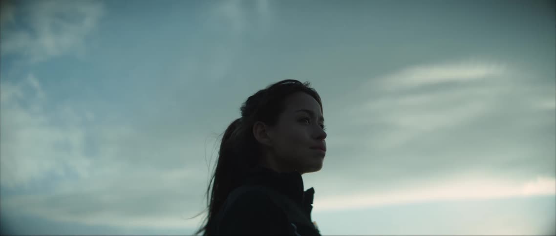 A woman is standing outside looking around under a cloudy sky