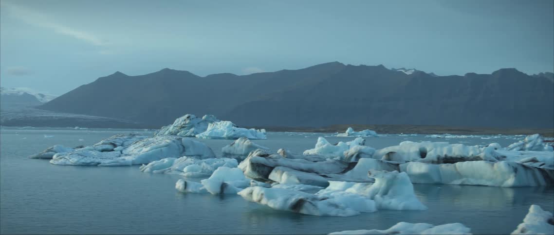 Icebergs float on water near shore with misty mountains in the background