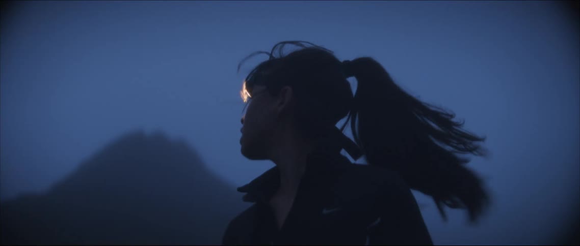 A woman with a headlamp looking around nervously while jogging in nature at night