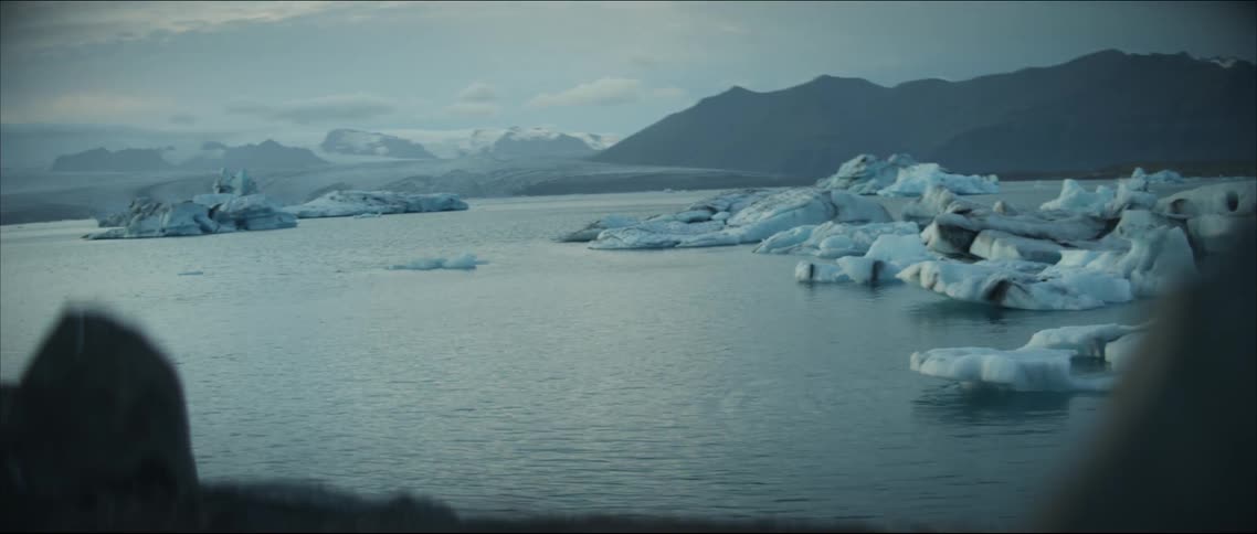 Broken icebergs dot the ocean near a mountain range