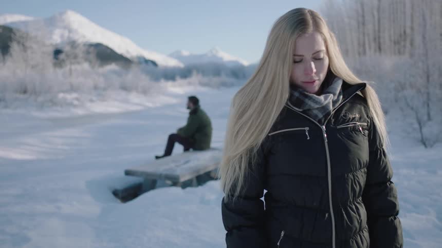 A blond woman standing in the snow looks up