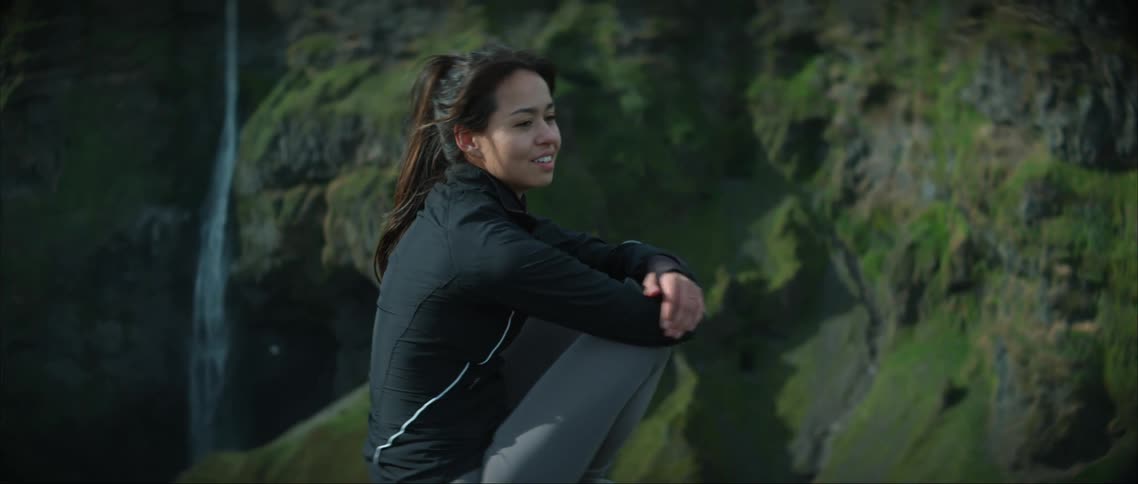 Woman sits on edge of canyon across from waterfall on opposite cliff