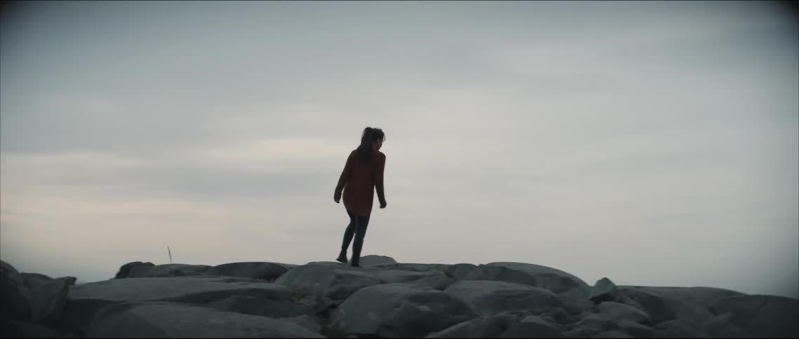A silhouetted woman walking over a rocky landscape in nature