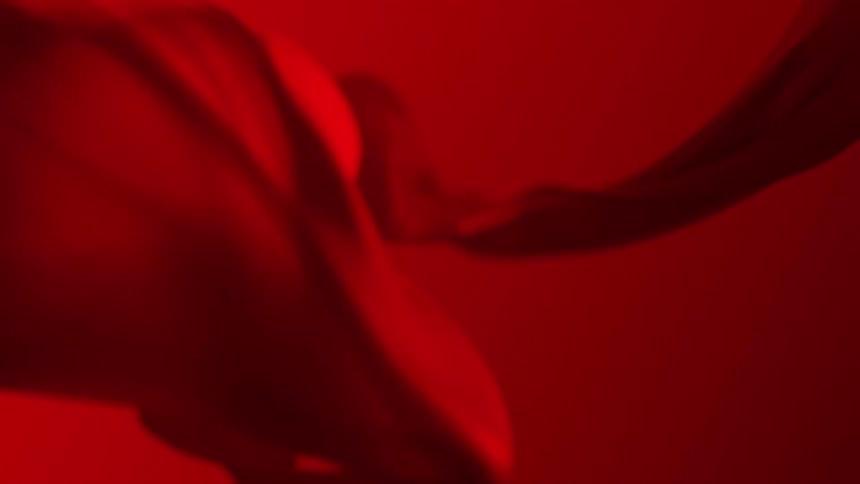 A red fabric is folding as it twists and turns as it floats in the air
