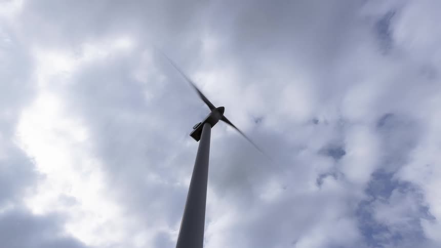 A time lapse shows the propeller of a wind turbine spinning swiftly under a cloudy sky