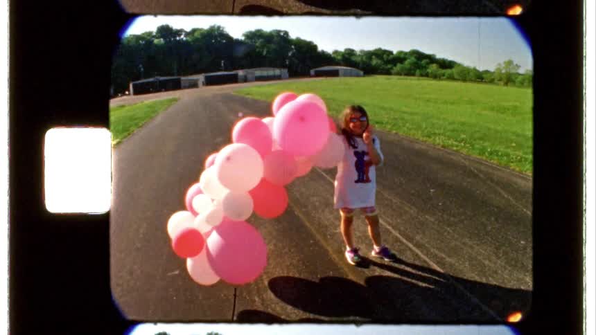 A girl runs up with a bunch of balloons