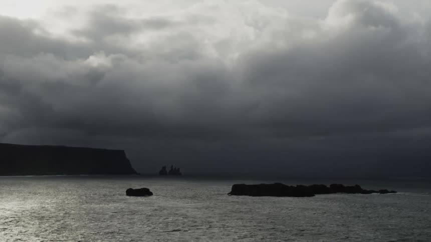 Thick clouds loom over a rocky coastline during the day