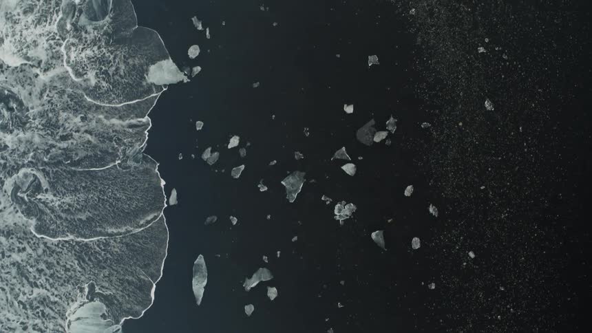 Top down aerial view of sheets of ice over the dark sand on a beach