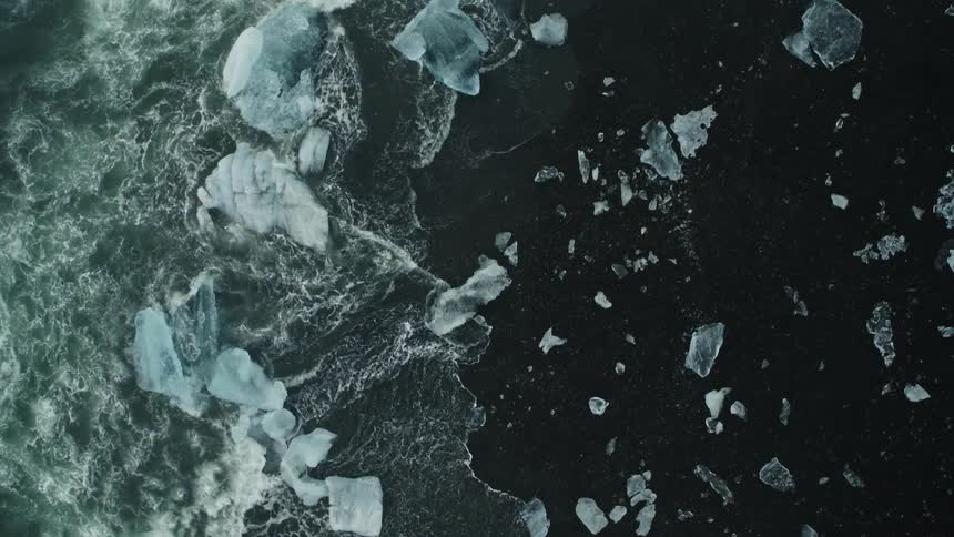 Waves splash and foam as they roll into shore and over pieces of melted ice