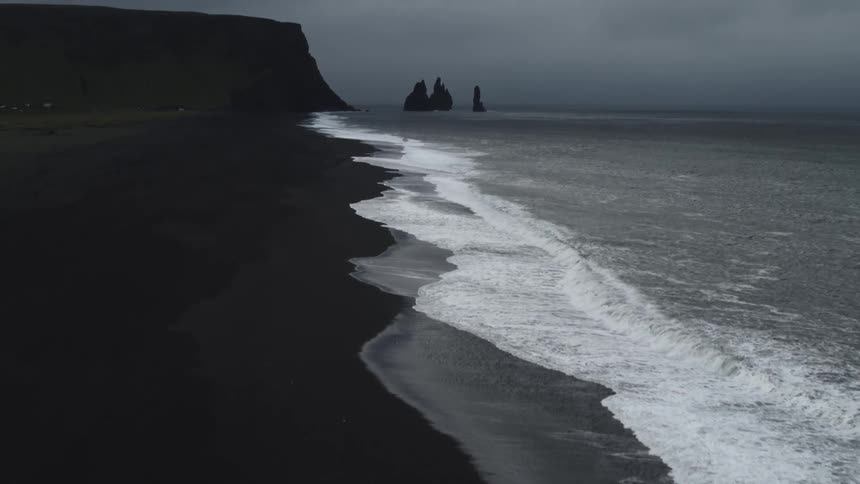 Numerous waves wash upon the sandy coastline under a very cloudy sky