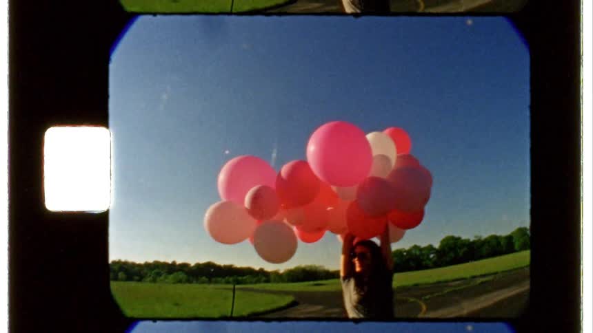 A woman holds up a dozen balloons while standing outside