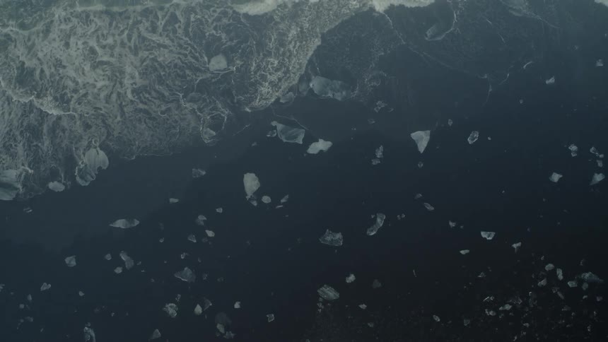 Waves splash and foam as they roll into shore and over pieces of melted ice