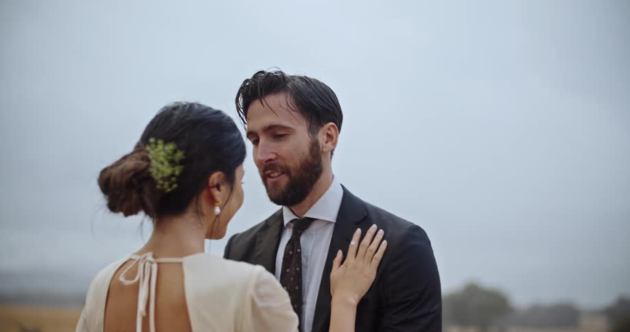 A man and woman wearing nice clothes stand together outdoors on a rainy day
