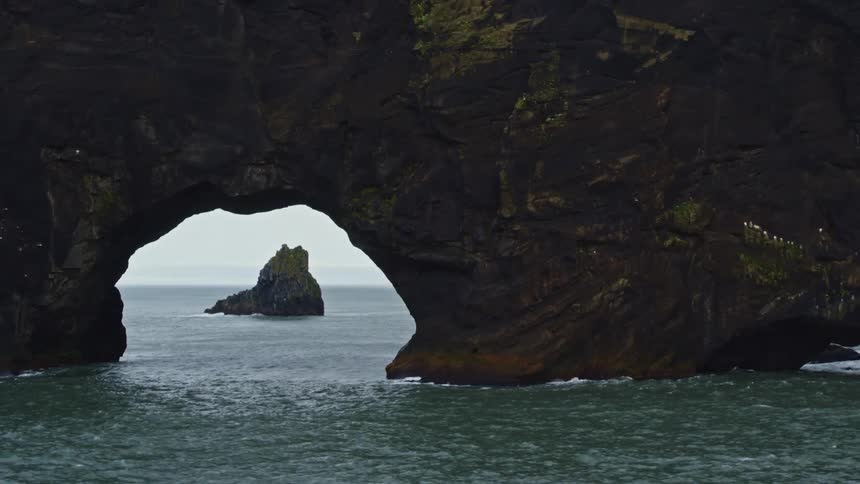Gentle waves move under arched rocks in the ocean